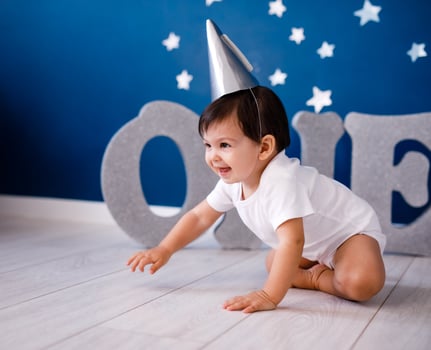 One year old baby boy in white t-shirt and silver hat celebrates birthday near silver letters ONE on purple background with stars photo
