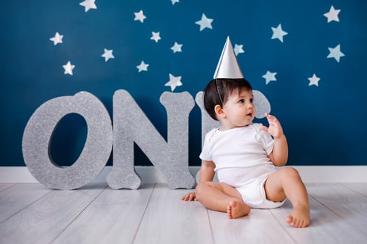 Baby boy of one year old wearing a white body and a festive paper hat sits on the floor on a blue background photo