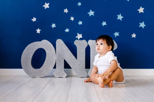 One year old baby boy in white t-shirt celebrates first birthday near silver letters ONE on blue background with stars photo