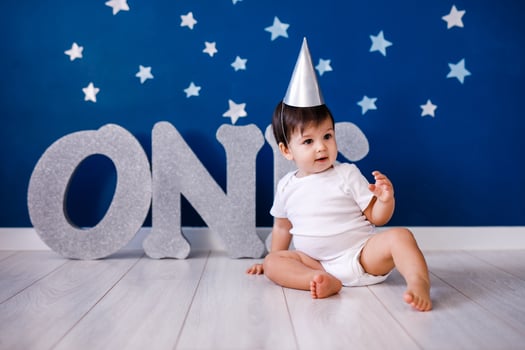 One year old baby boy in white t-shirt and silver hat celebrates birthday near silver letters ONE on purple background with stars photo