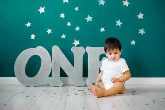 One year old baby boy celebrates birthday near silver letters ONE on blue background with stars photo