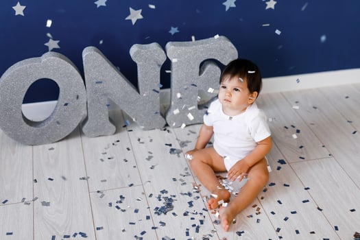 One year old baby boy in white t-shirt celebrates birthday near silver letters ONE on blue background with stars and silver sparkles. photo