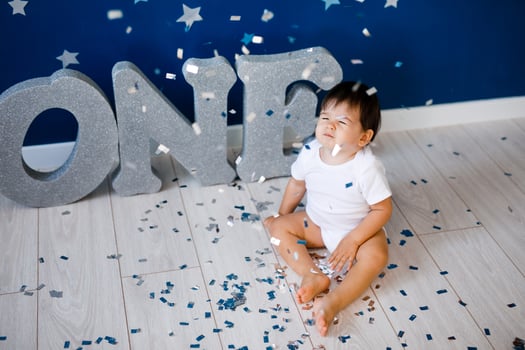 One year old baby boy in white t-shirt celebrates birthday near silver letters ONE on blue background with stars and silver sparkles. photo