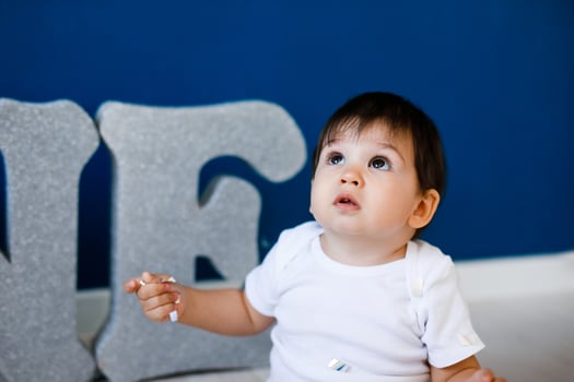 One year old baby boy celebrates birthday near silver letters ONE on blue background with stars photo