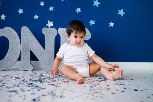 One year old baby boy in white t-shirt celebrates birthday near silver letters ONE on blue background with stars and silver sparkles. photo