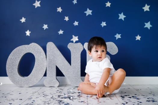 One year old baby boy in white t-shirt celebrates birthday near silver letters ONE on blue background with stars and silver sparkles. photo