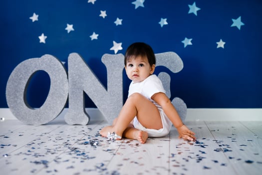 One year old baby boy in white t-shirt celebrates birthday near silver letters ONE on blue background with stars and silver sparkles. photo