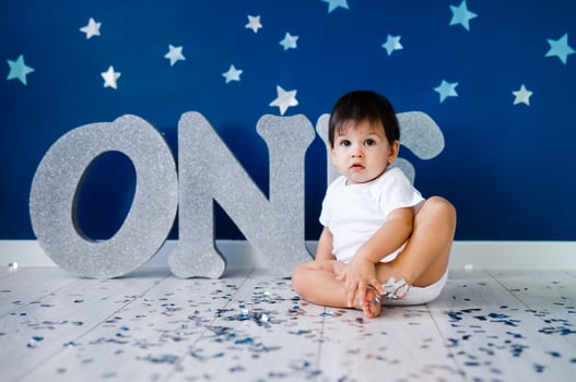 One year old baby boy in white t-shirt celebrates birthday near silver letters ONE on blue background with stars and silver sparkles. photo