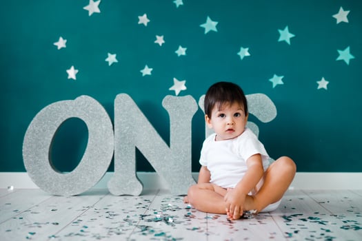 One year old baby boy in white t-shirt celebrates first birthday near silver letters ONE on green background with stars photo
