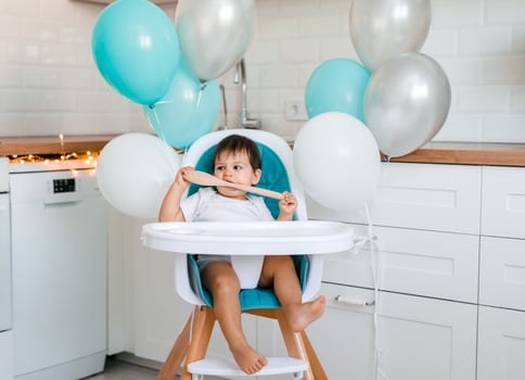 A one-year-old boy is seen in the kitchen in a high chair with a wooden spoon in his hands photo