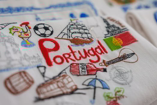 Intricately stitched fabric featuring the word Portugal, a rooster, a soccer ball, a tram, a ship, an umbrella, and the Portuguese flag, representing Portuguese heritage. photo
