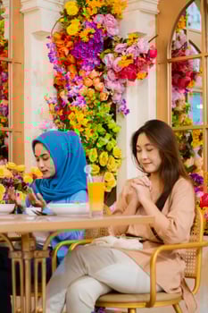 portrait of diversity 2 beautiful young indonesia female smiling praying devoutly before eating sitting on chairs in an indoor restaurant. for the concept of religion, lifestyle, worship, advertising photo