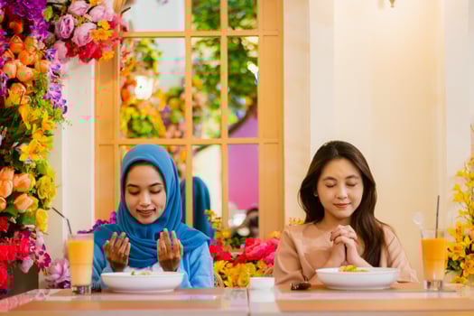 diversity 2 beautiful young asian girl smiling praying before eating sitting on chairs in an indoor restaurant. for the concept of religion, lifestyle, worship, advertising photo