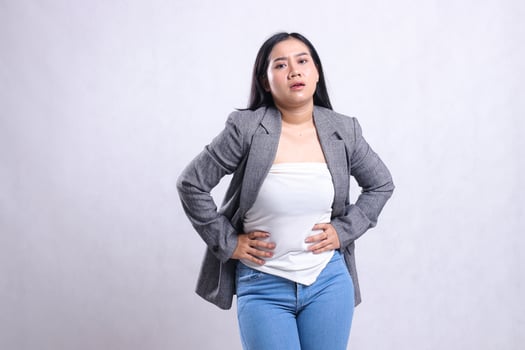 gesture of beautiful young woman asia with stomachache wearing grey jacket and jeans standing isolated on white background. for health, treatment, commercial, prevention content photo