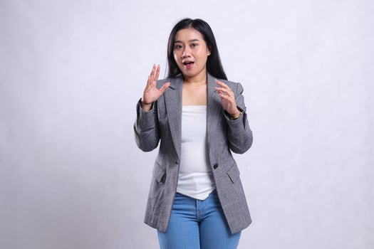 expression of beautiful young woman surprised smiling both arms spread in front of chest wearing grey jacket and jeans standing isolated on white background. for advertising content, fashion, magazine photo
