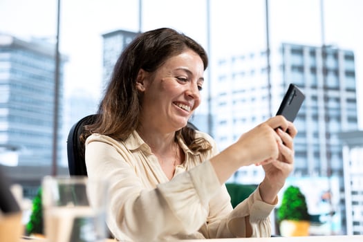 Pleased empowered businesswoman texting messages in her own director office, having fun on social media. Leader discussing with partners about new project ideas for career growth. photo