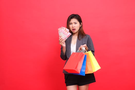 The indonesia female customer was surprised to be carrying rupiah notes and various shopping paper bags wearing a gray suit with a red background. for transaction, lifestyle and business concepts photo