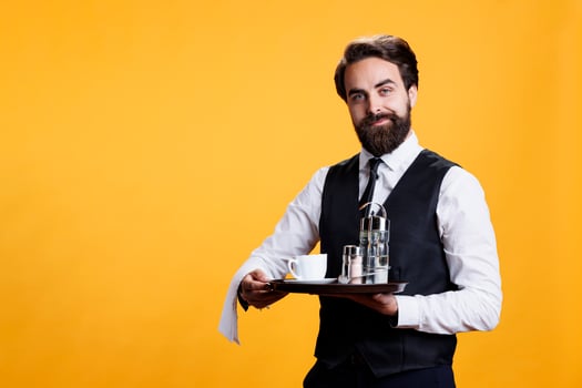 Stylish waiter carrying tray with coffee and cutlery to serve people at five star restaurant, luxurious catering employee with towel over arm. Professional butler with suit and tie holds platter. photo