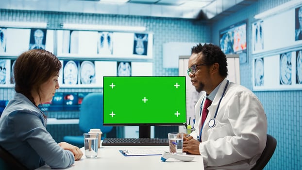 African american medic points at green screen on computer while he consults his patient, exploring treatment plans on health insurance. Physician gives medical advice to ill woman. Camera B. photo
