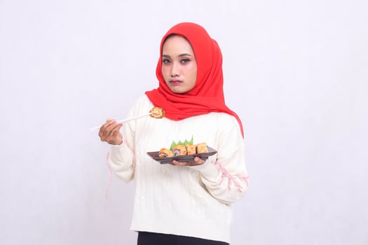 indonesia woman wearing a hijab pouts at the camera, picking up chopsticks and carrying a plate containing sushi Japanese food. Beautiful Muslim women are used for food and advertising content photo