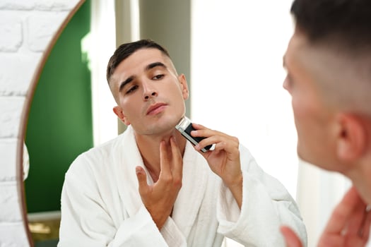 Reflection of a young man shaving in bathroom mirror close up photo