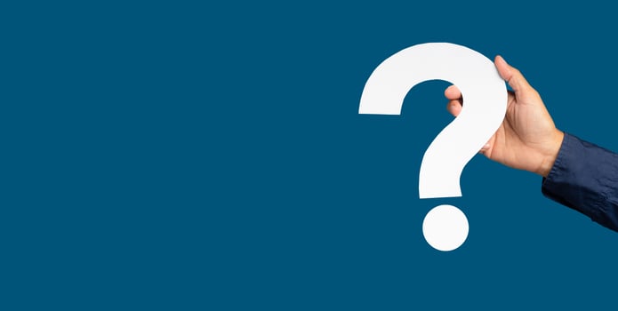 Hand holding a white question mark paper while standing on a blue background. photo