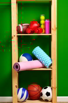 Shelves with different sports equipment against green wall photo