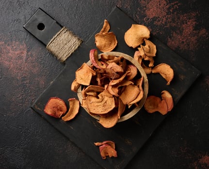 Dried apple pieces in a wooden round plate on a black table photo