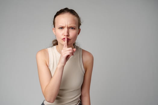 Young Woman Making a Hush Gesture on gray background in studio photo