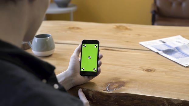 View over the shoulder of a businessman using the hand held cellphone with green screen touchpad on wooden table background. Stock footage. Man lloking at his device, chromakey. photo