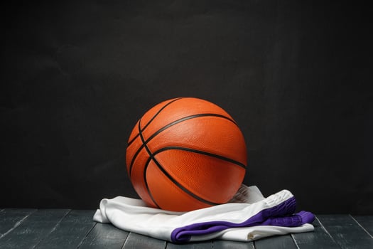 Vibrant Orange Basketball Resting on a Dark Wooden Floor With White and Purple uniform photo