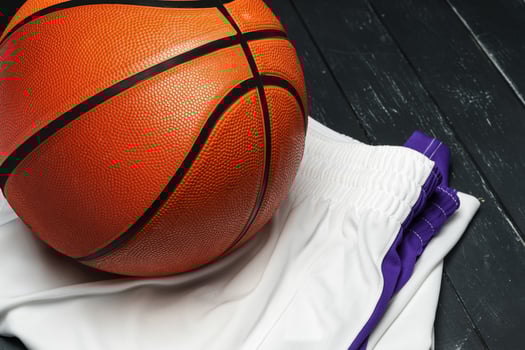 Vibrant Orange Basketball Resting on a Dark Wooden Floor With White and Purple uniform photo