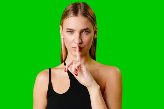 Young Woman Gesturing Silence With Finger on Lips Against Green Screen Background photo