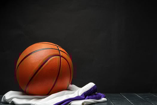 Vibrant Orange Basketball Resting on a Dark Wooden Floor With White and Purple uniform photo