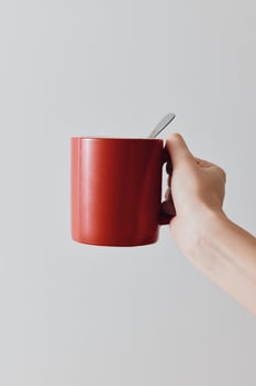 Red coffee mug and spoon in hand on white background. copy space available. great for coffee lovers photo