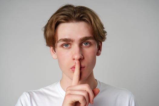 Young Man With Finger on Lips Signaling Silence Against a Plain Background photo