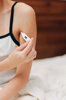Woman holding thermometer sitting on bed in morning. photo