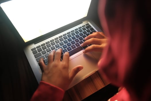 A person is intently focused on typing on a laptop while sitting in a dimly lit environment photo