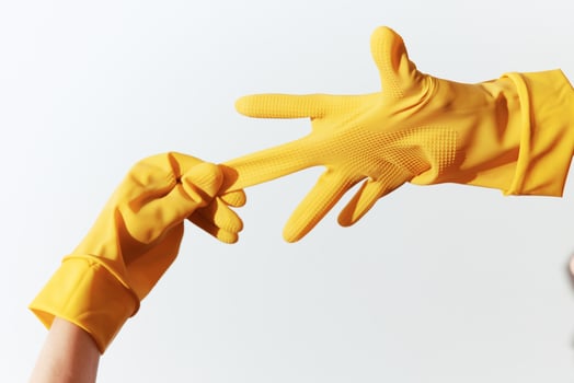 Two individuals wearing yellow rubber gloves reaching out to each other on a white background. photo