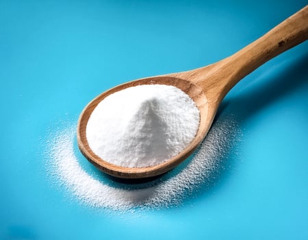 Baking soda in wooden spoon isolated on light blue background photo
