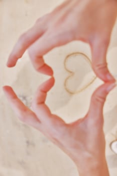 Hands making heart shape with sand on white countertop, holding pair of scissors. photo