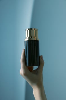 Elegant black and gold perfume bottle held by hand on blue background with copy space in top left photo