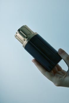 Man holding a black and gold bottle and a lighter against a blue sky. photo