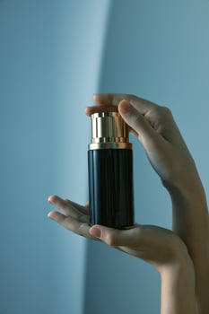 Hand holding black and gold perfume bottle on blue background with copy space. elegance and luxury photo