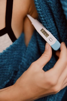 Woman holding electronic thermometer, wearing blue shirt, holding blue towel on arm. photo