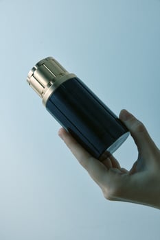 Hand holding luxurious black and gold perfume bottle on blue background, close up shot with space photo