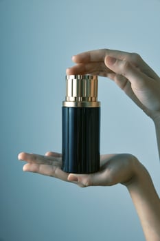 Black and gold perfume bottle being held by a person, with empty space in the top right corner of photo