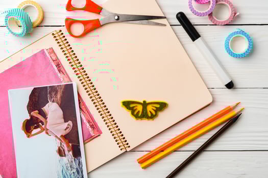 Colorful stationery arrangement with a butterfly sticker on a blank notebook at a wooden table in natural light photo