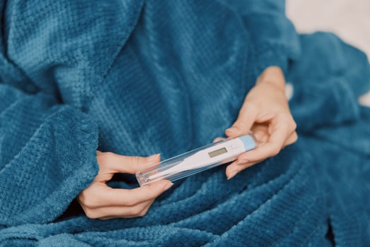 Woman holding thermometer wrapped in blue blanket, wearing blue shirt and pajama pants photo