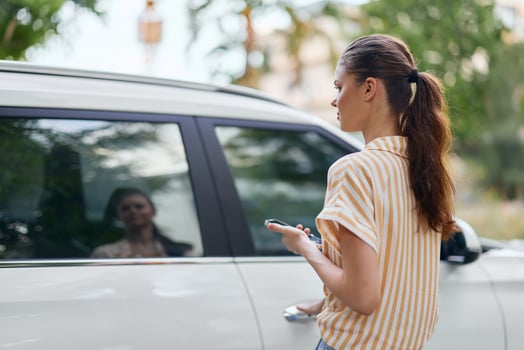 Outdoor lifestyle image of a woman standing beside a car while checking her phone She has long hair photo